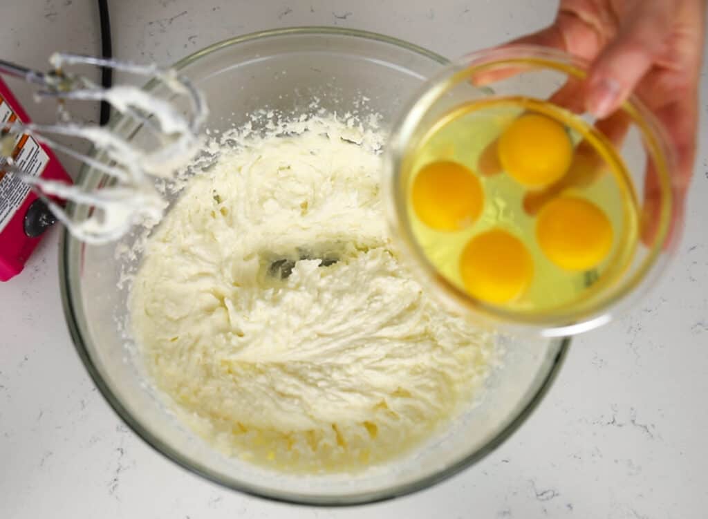 eggs being added to bowl of creamed vanilla cake batter