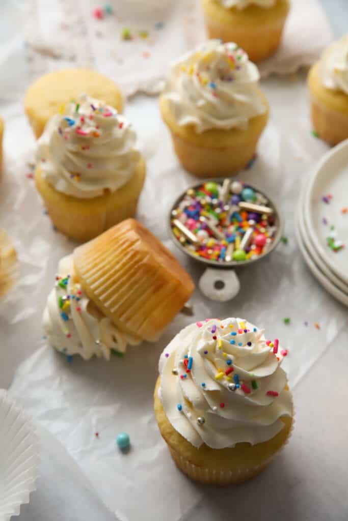 vanilla cupcakes with vanilla frosting and a dish of sprinkles