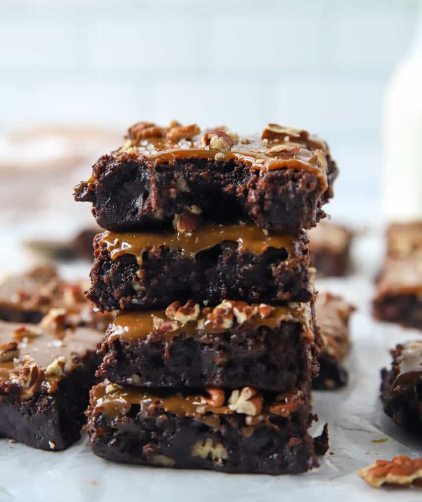 four caramel turtle brownies stacked on top of each other