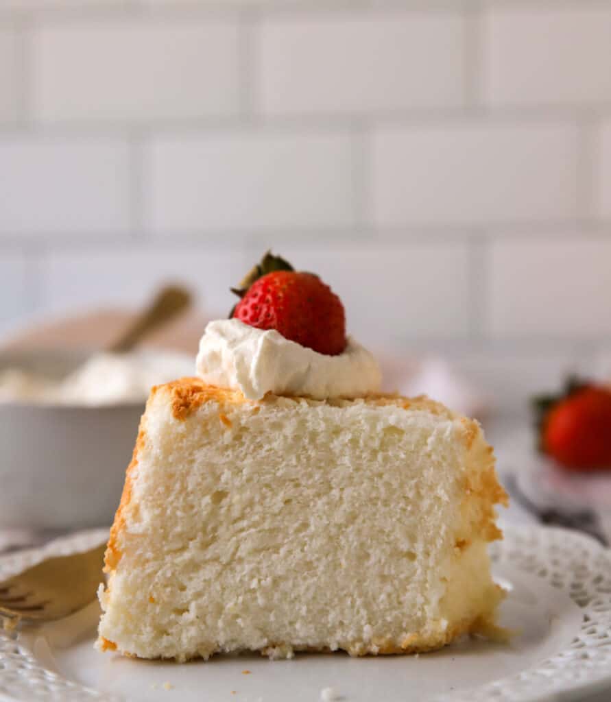 slice of angel food cake upright on a plate topped with whipped cream and a strawberry