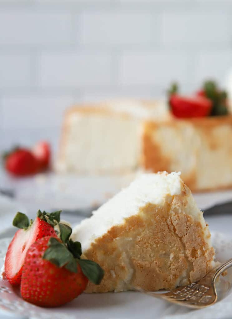 slice of angel food cake on a plate with strawberries, and angel food cake in background