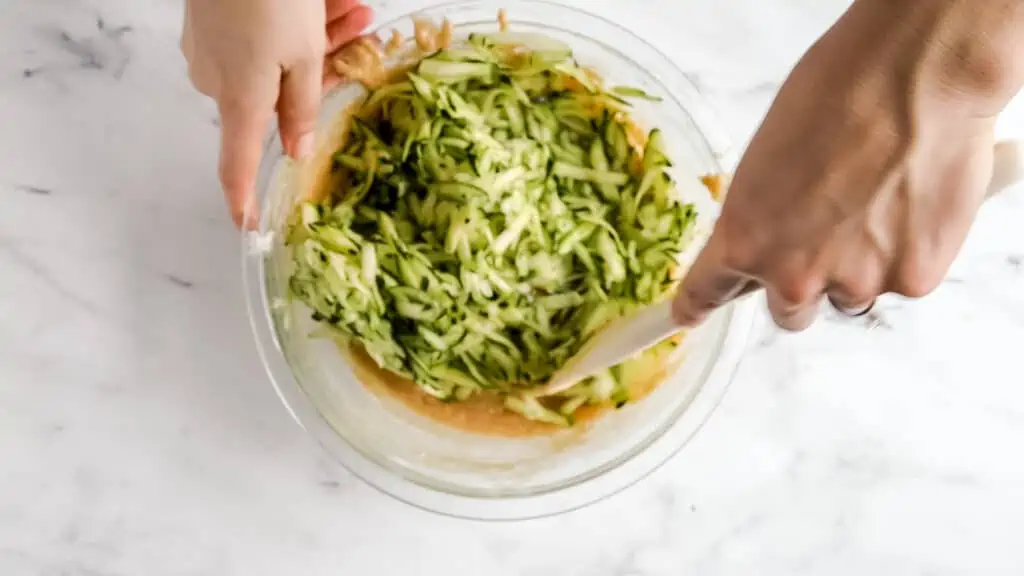hand whisking shredded zucchini into the batter in a bowl