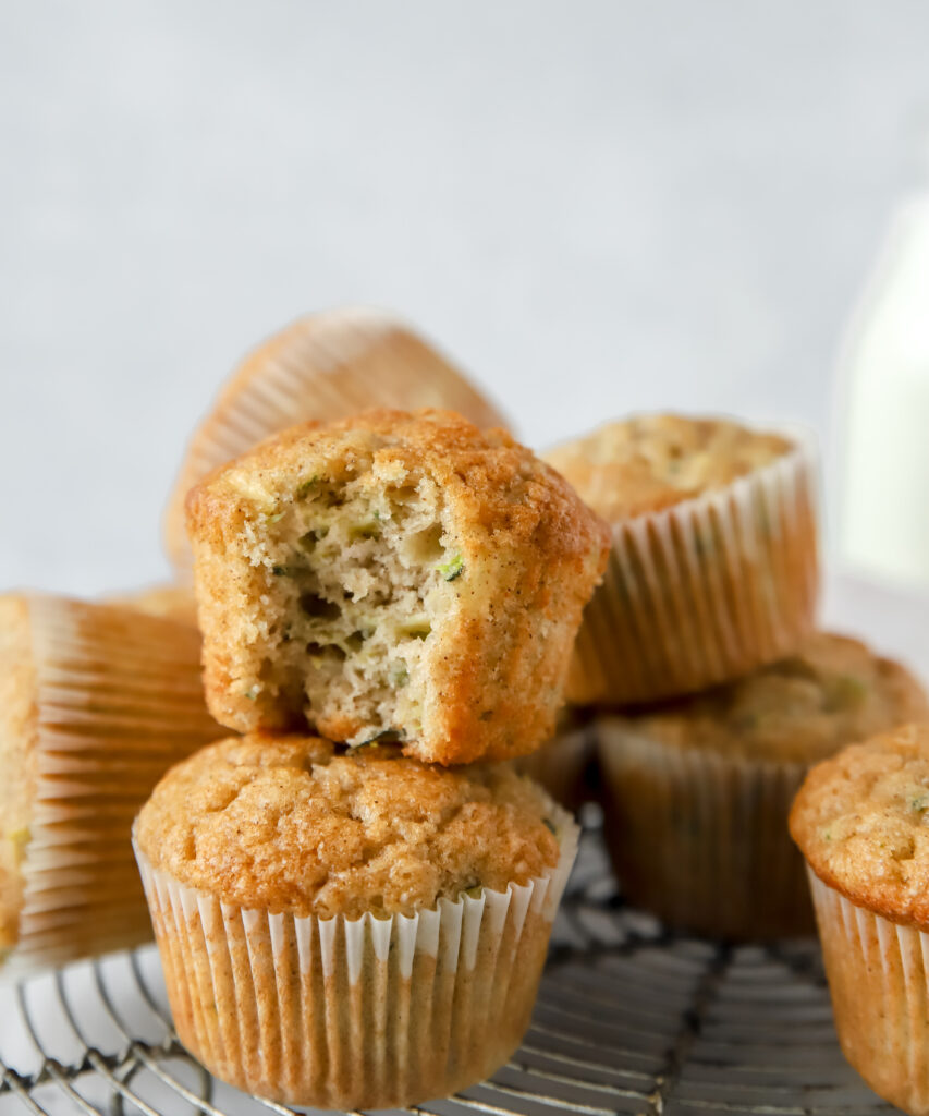 two zucchini muffins stacked on each other, the top muffin has a bite taken out of it