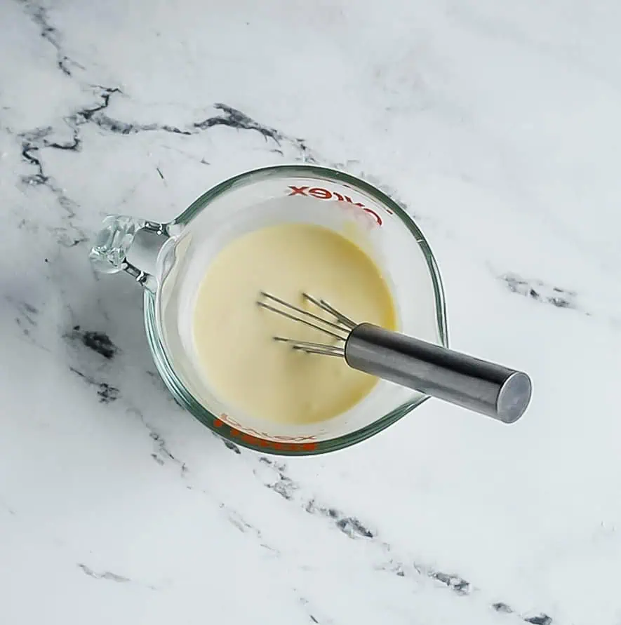 measuring cup with whisked heavy cream, egg, and vanilla in it, and small whisk in the cup