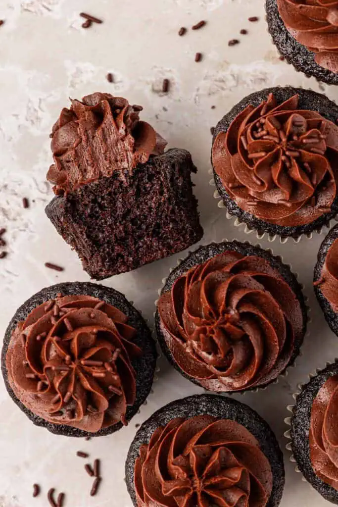 a bunch of chocolate cupcakes with one cut in half on its side