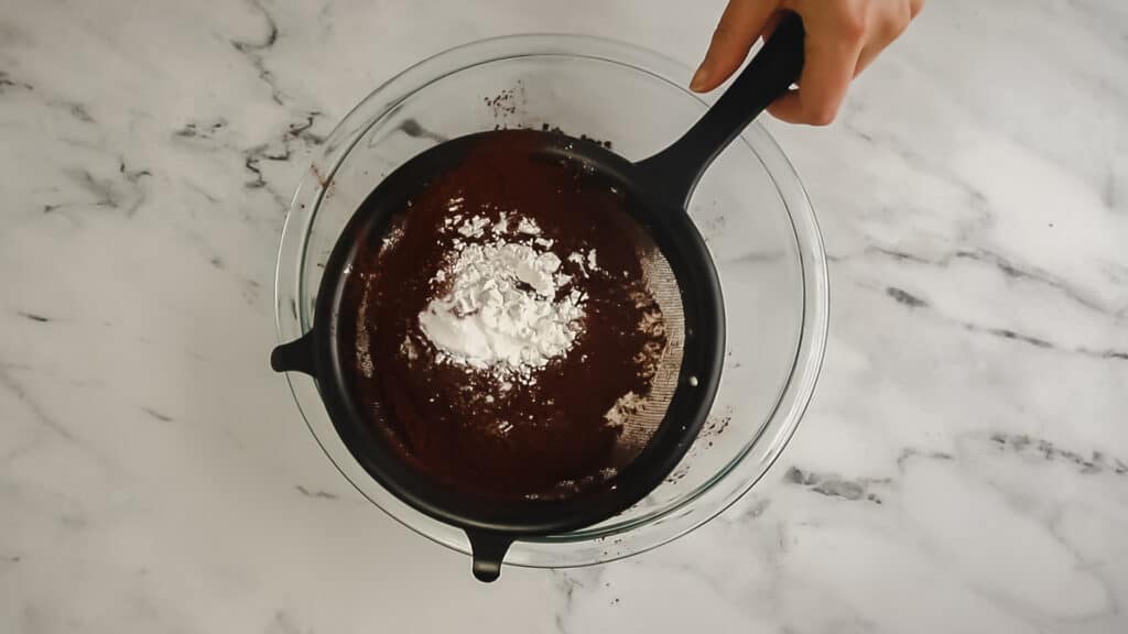 chocolate layer cake dry ingredients being sifted over a glass bowl