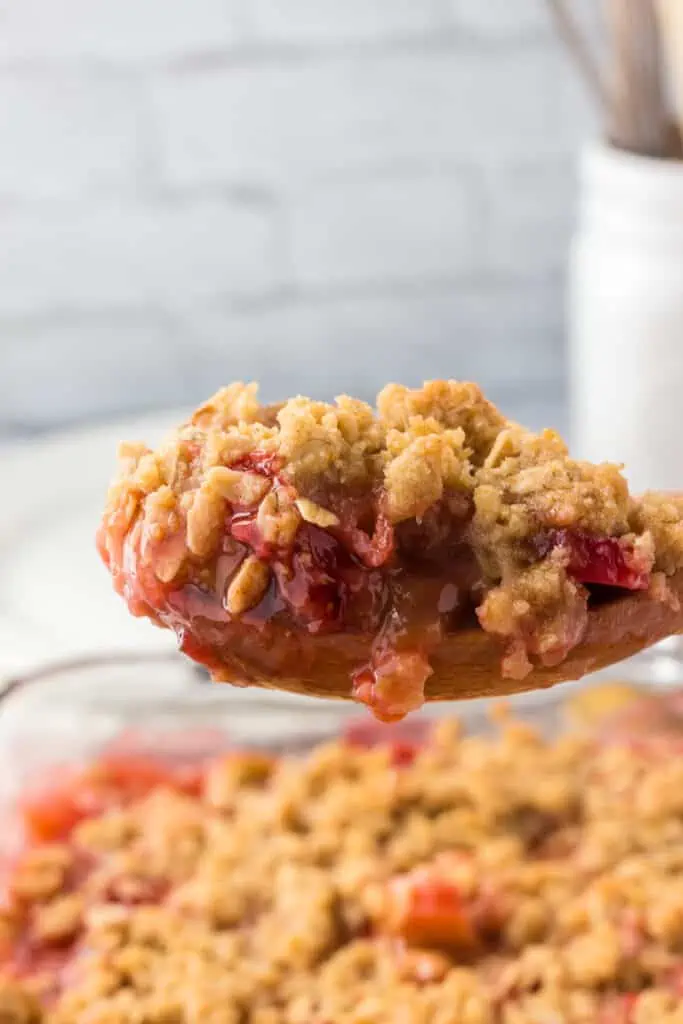 wooden spoon holding a spoonful of strawberry rhubarb crisp