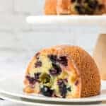 blueberry pound cake slice on a plate with bundt cake in background