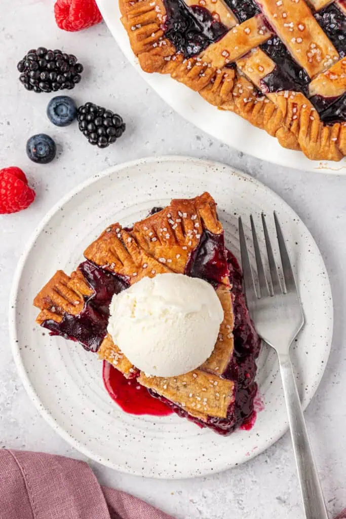 slice of berry pie on a plate topped with ice cream