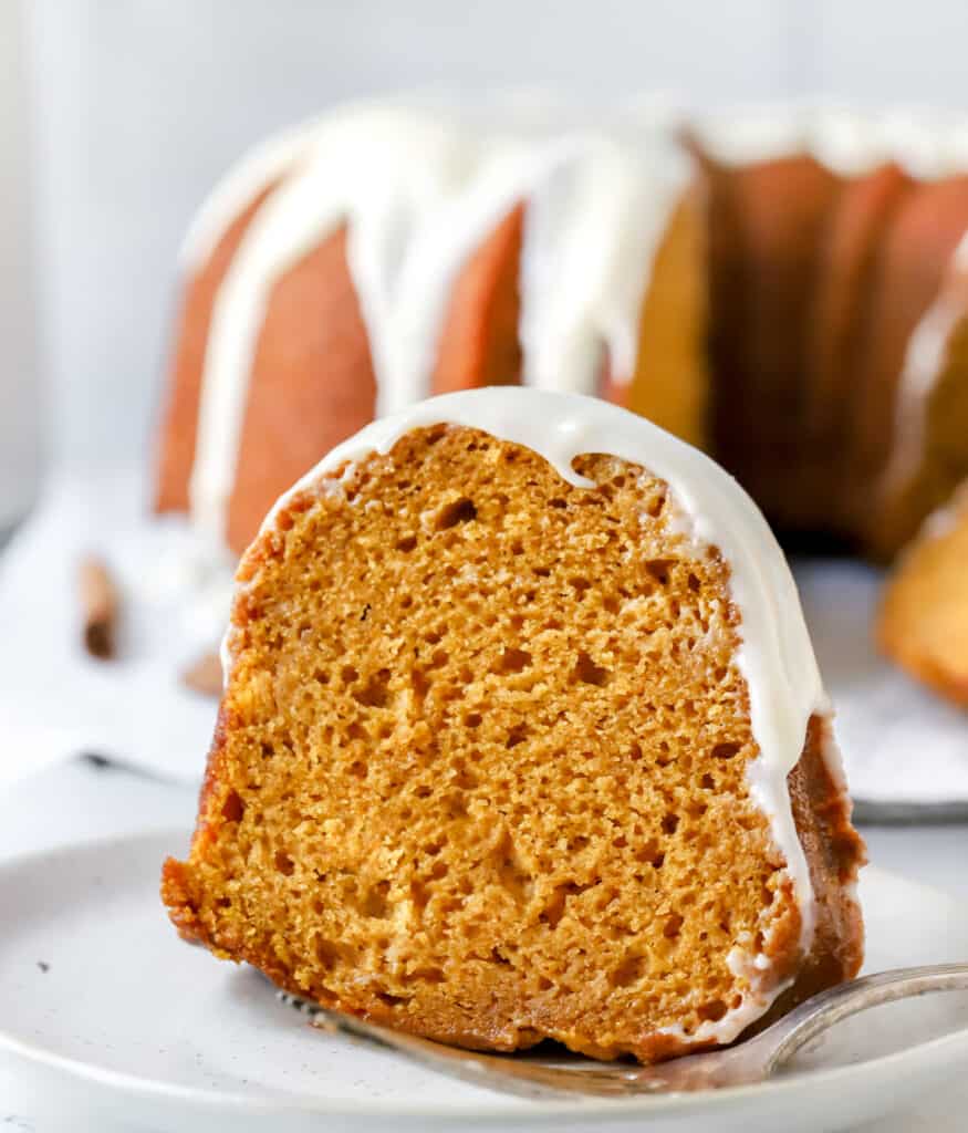 slice of pumpkin bundt cake on a plate with bundt cake in the background