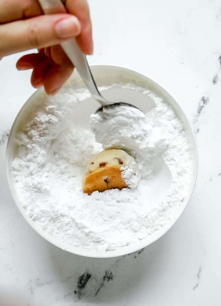 spoon rolling a Russian tea cake cookie in a bowl of powdered sugar
