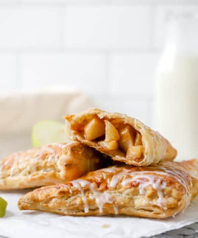 two apple turnovers stacked, one puff pastry apple turnover cut in half