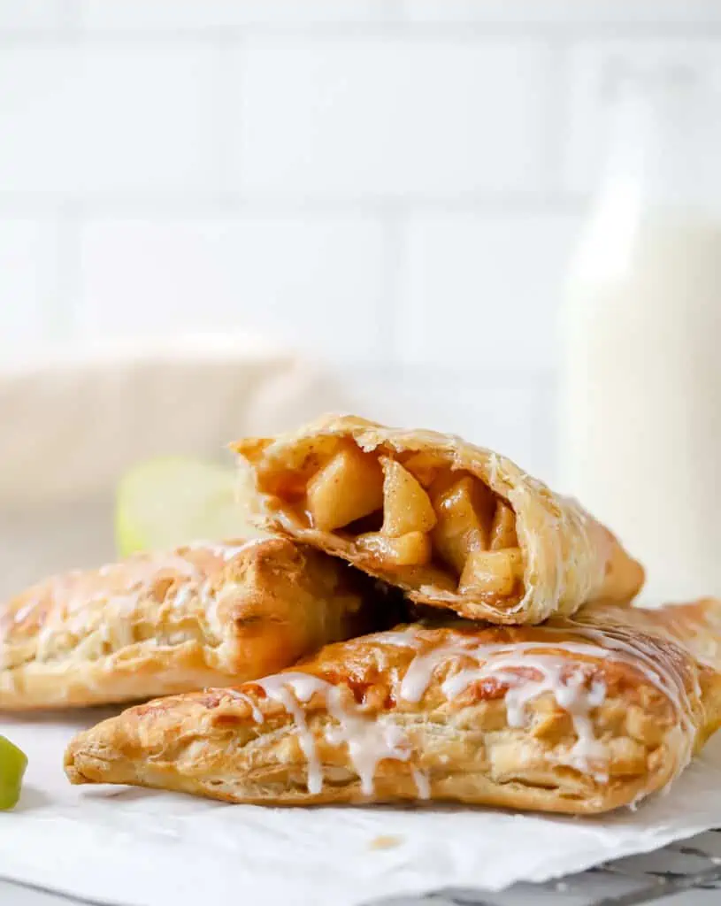 two apple turnovers stacked, one puff pastry apple turnover cut in half