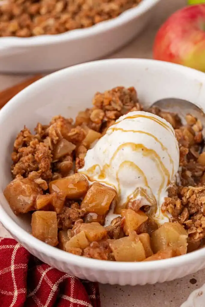 bowl of apple crisp topped with a scoop of ice cream and caramel sauce