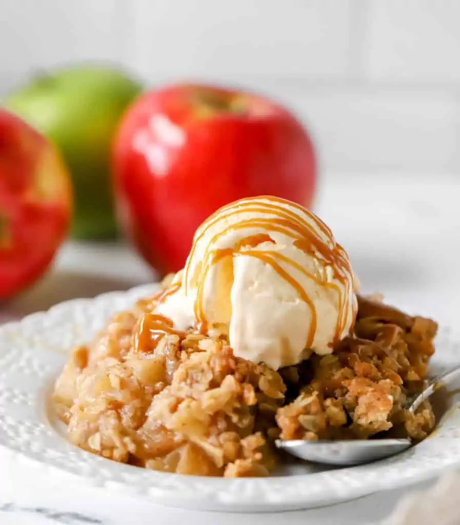 white plate with apple crisp on it topped with vanilla ice cream