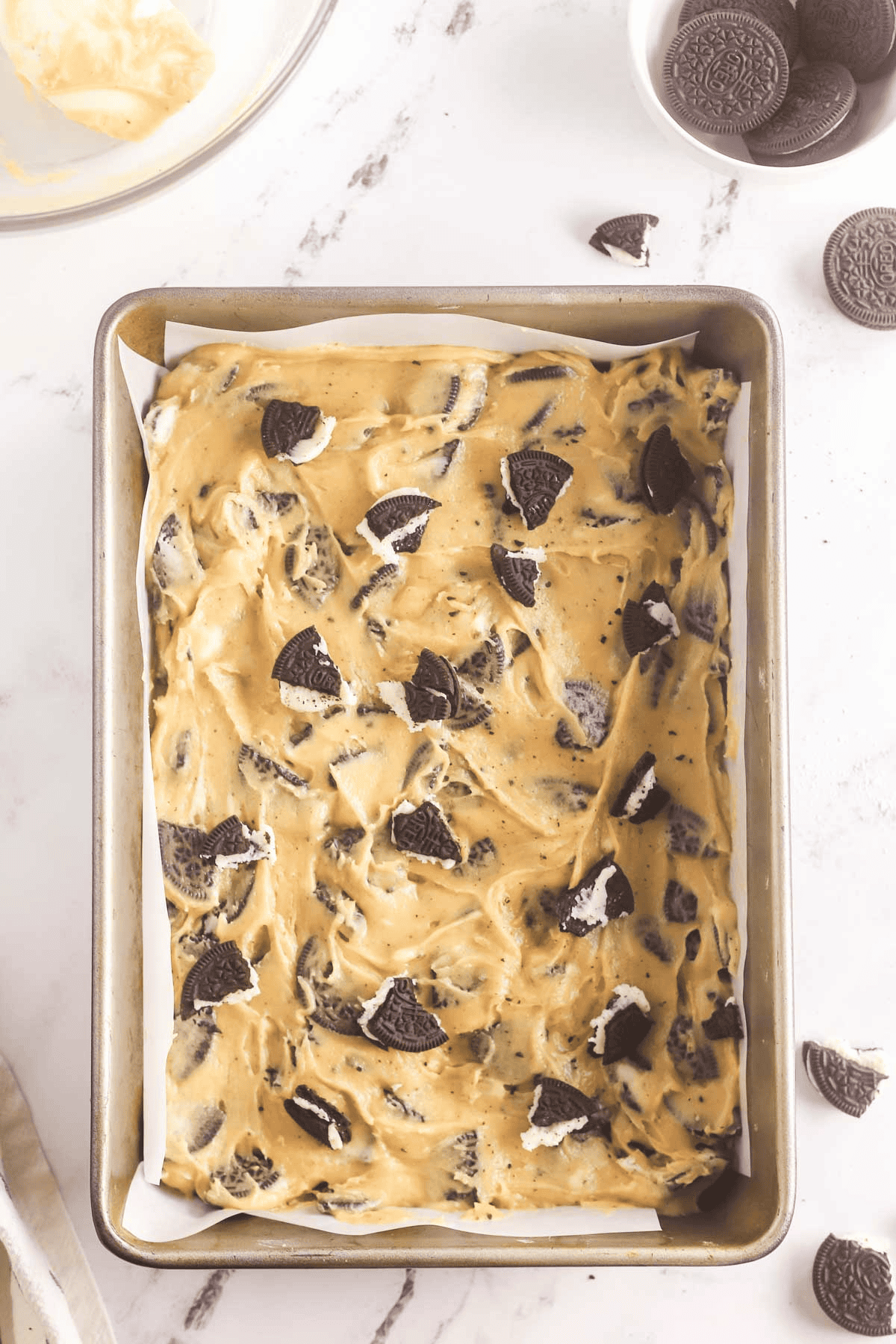 unbaked Oreo blondies in a 9x13 parchment paper lined pan with chopped Oreos on top