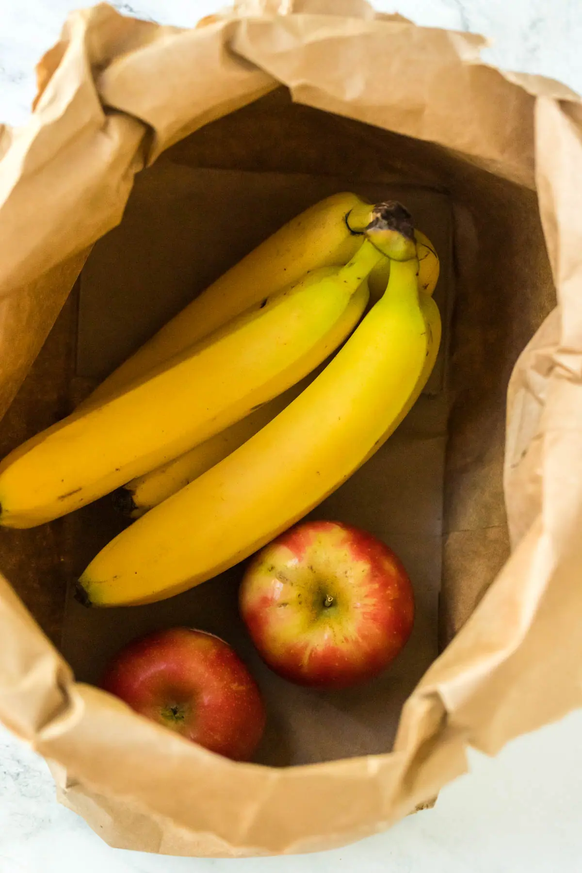 a bunch of bananas and two apples in a brown paper bag