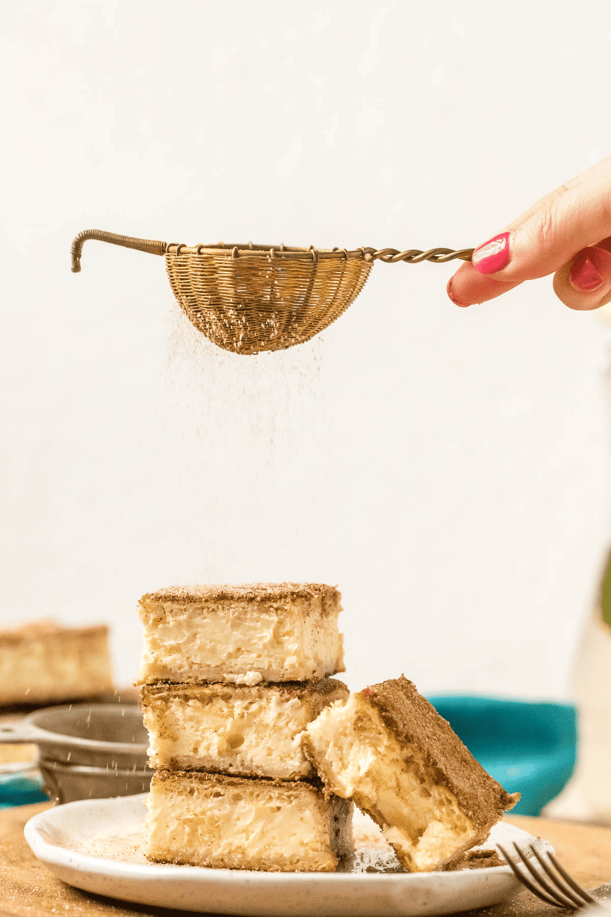 gold sifter sifting cinnamon sugar over a stack of churro cheesecake bars