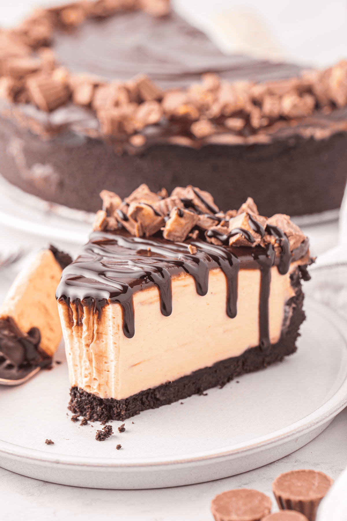 slice of no bake peanut butter cheesecake on a plate topped with hot fudge and reese's peanut butter cups with a bite missing