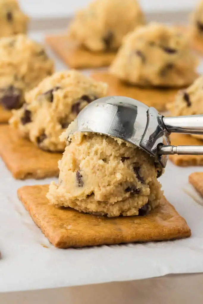 cookie scoop scooping chocolate chip cookie dough on top of a graham cracker