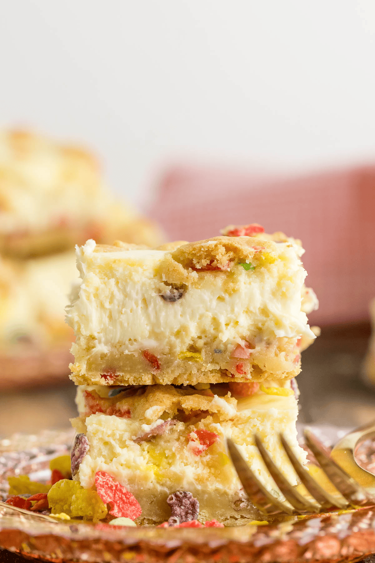 two fruity pebble cheesecake bars stacked on a plate with a fork