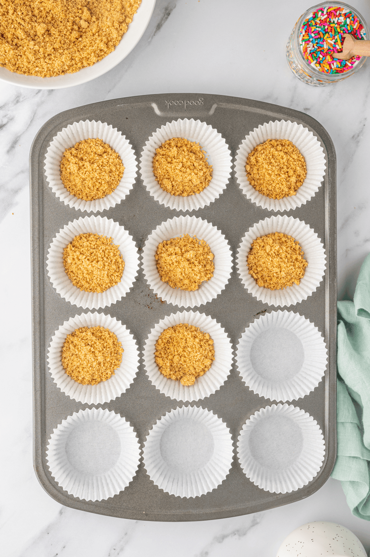 graham cracker crust mixture in bottom of muffin cups in a muffin pan