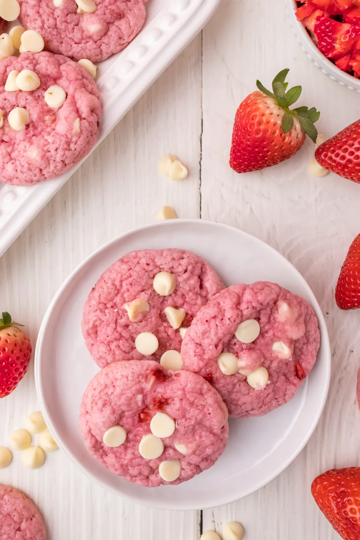 three strawberry white chocolate chip cookies topped with white chocolate chips on a plate