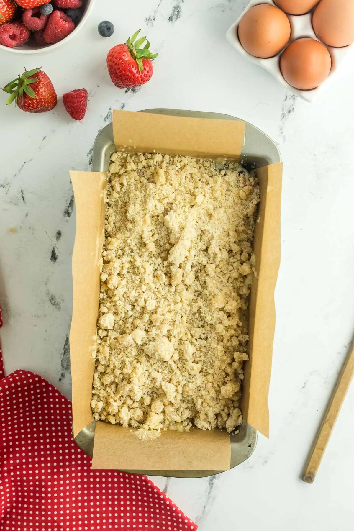 streusel sprinkled on top of berry bread batter in prepared pan