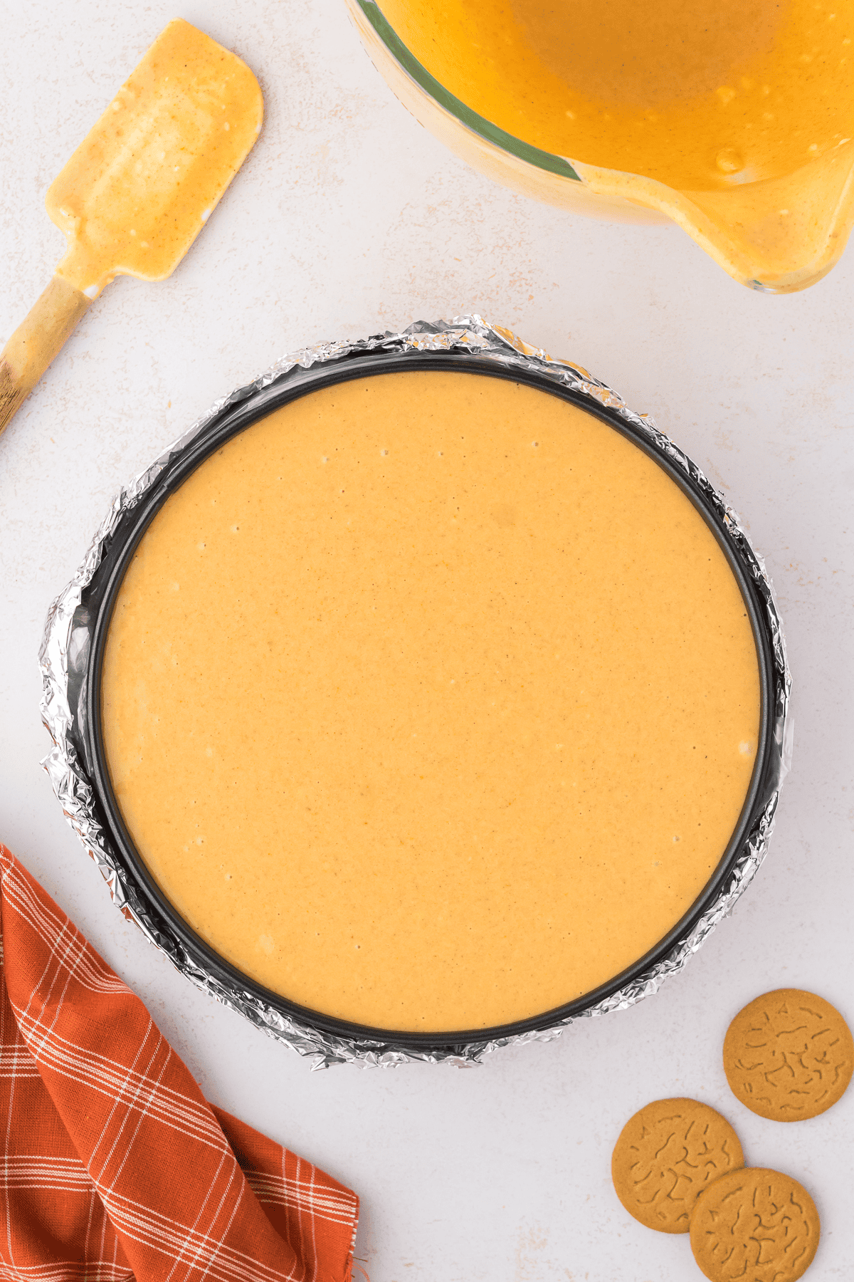pumpkin cheesecake filling in a springform pan wrapped in aluminum foil