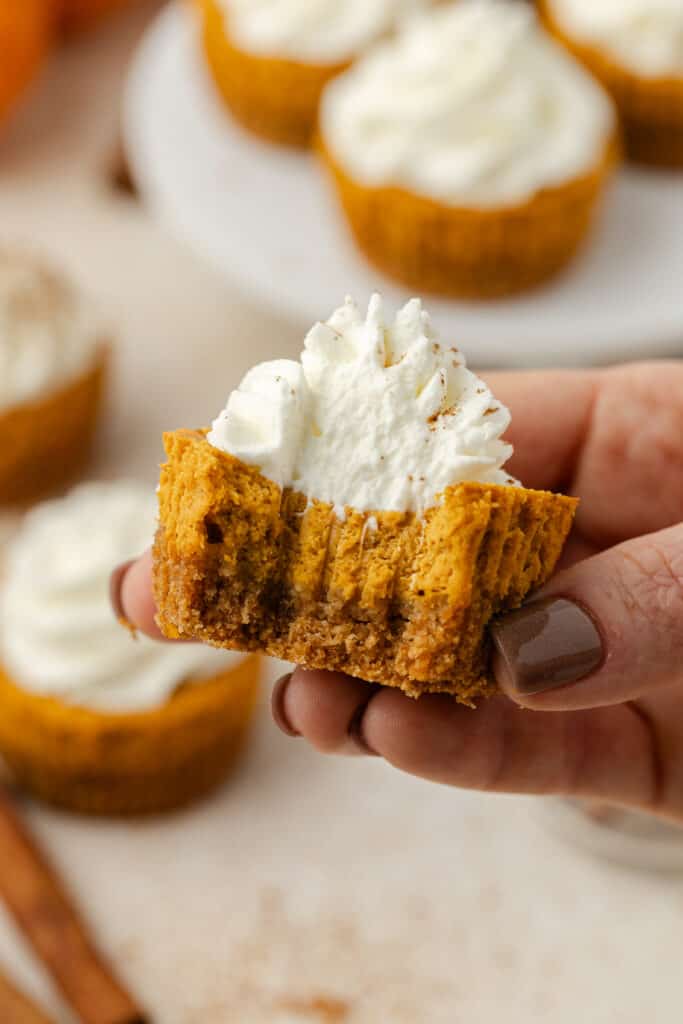 hand holding a mini pumpkin cheesecake with a bite taken out of it