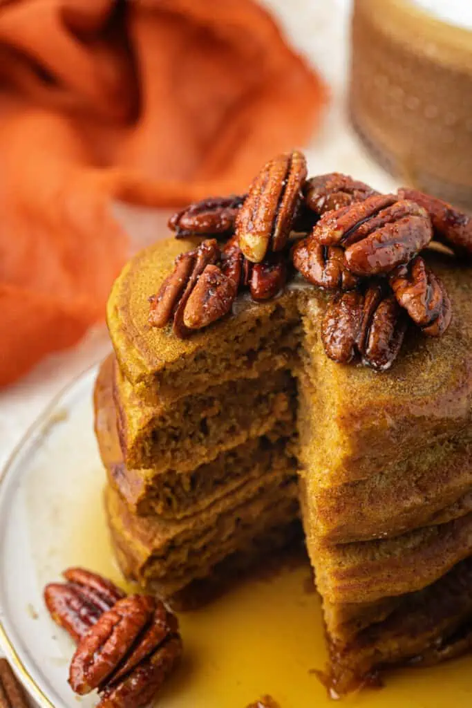 stack of pumpkin pie pancakes topped with pecans and a bite missing