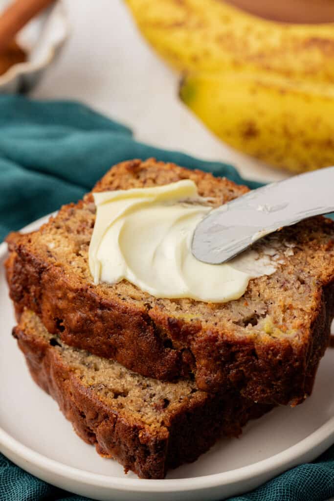 butter knife spreading butter on a slice of buttermilk banana bread