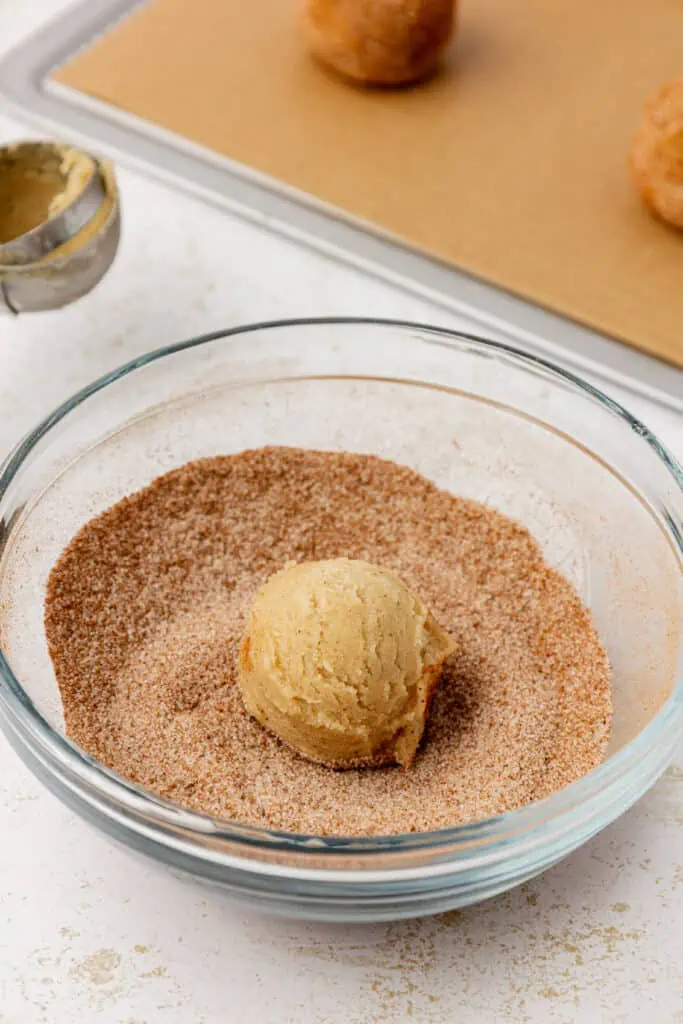 chai snickerdoodle cookie dough ball in a bowl of chai sugar mixture
