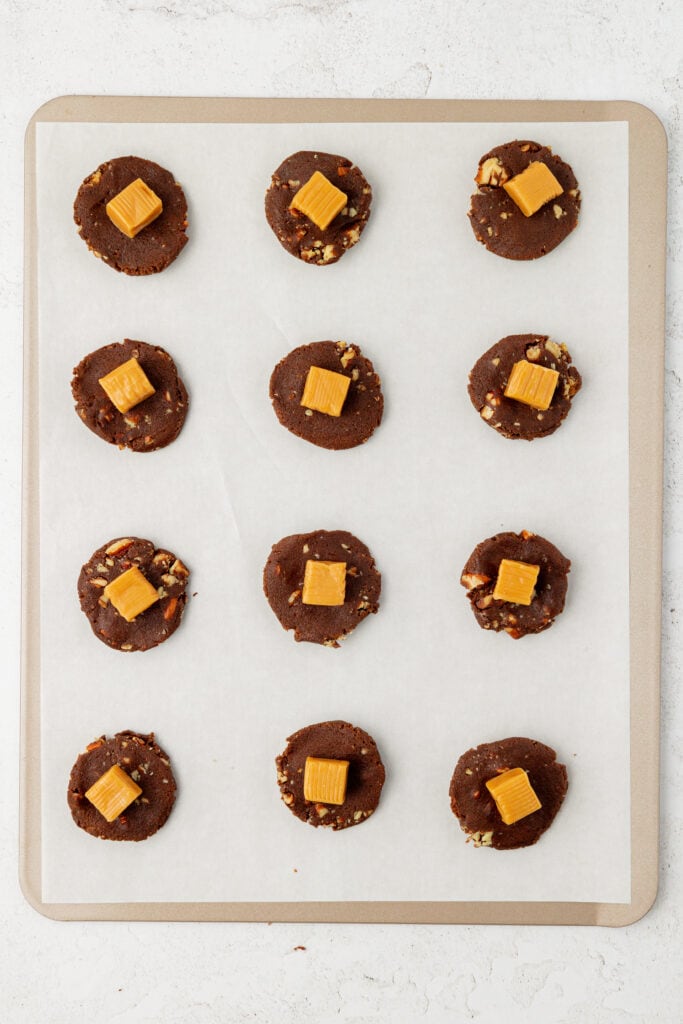 caramels in the middle of a chocolate cookie dough ball ona cookie sheet