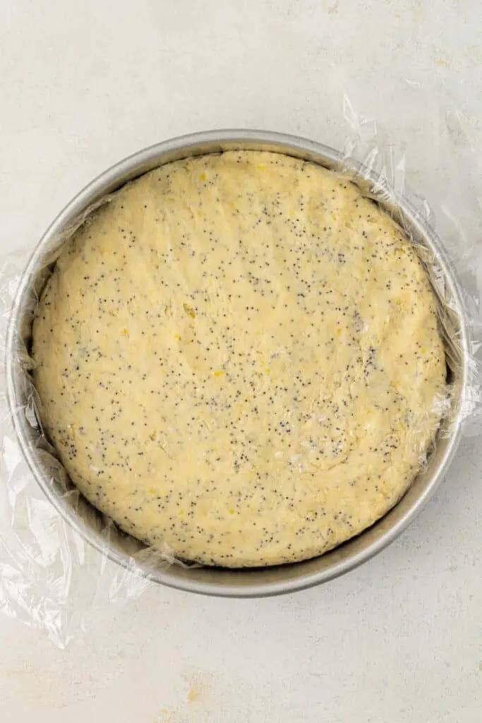 lemon poppyseed scone dough shaped into a cake pan lined with plastic wrap
