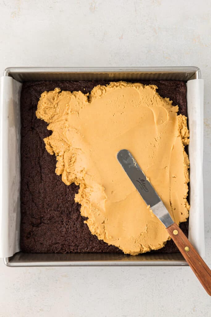 peanut butter being spread over the top of the brownies