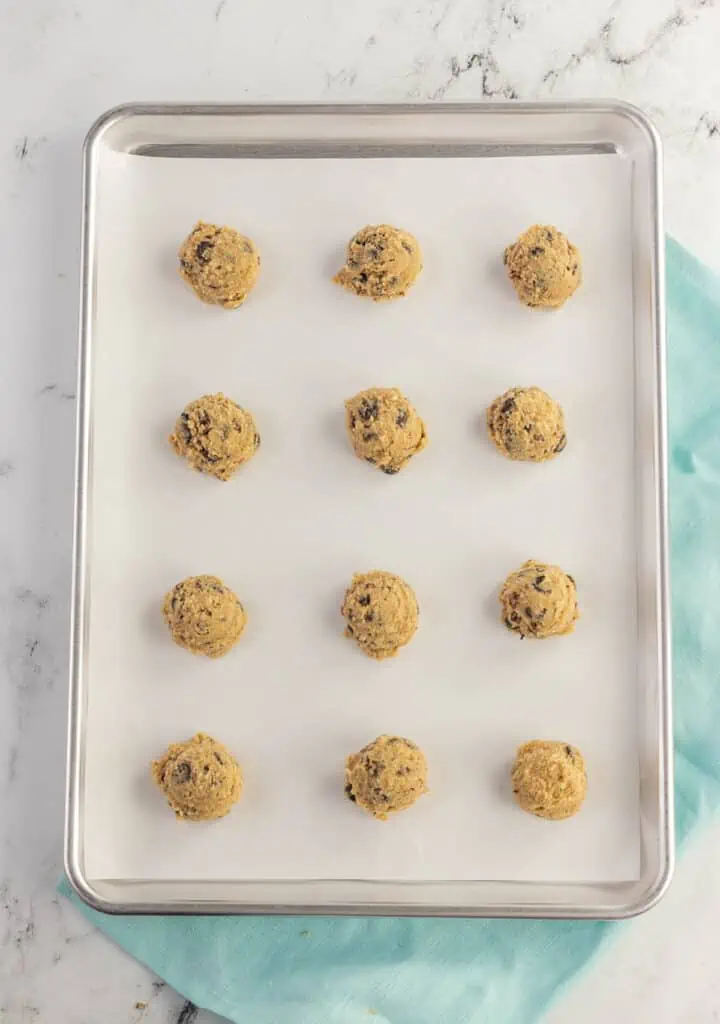 twelve chocolate chip pecan cookie dough balls on a baking sheet