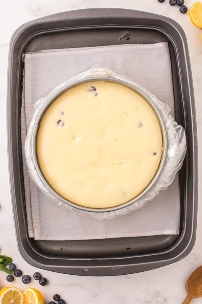 lemon blueberry cheesecake batter in a springform pan and wrapped in a plastic bag