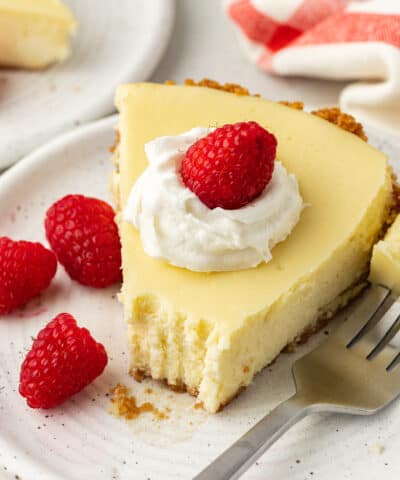 slice of cheesecake pie on a plate topped with whipped cream and raspberries