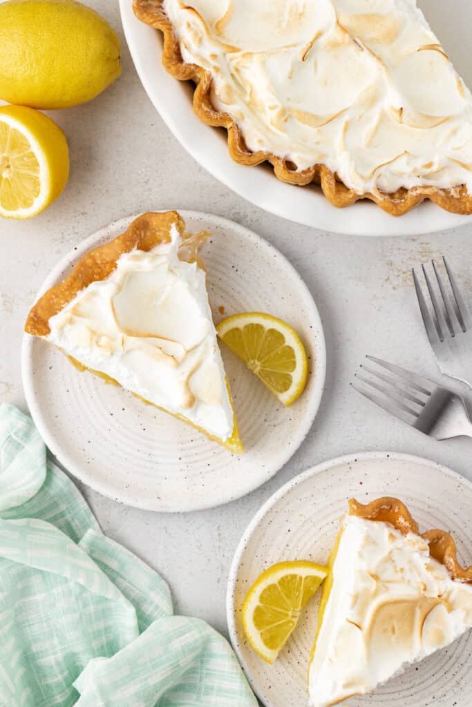 two slices of lemon meringue pie next to a whole lemon meringue pie in a pie plate