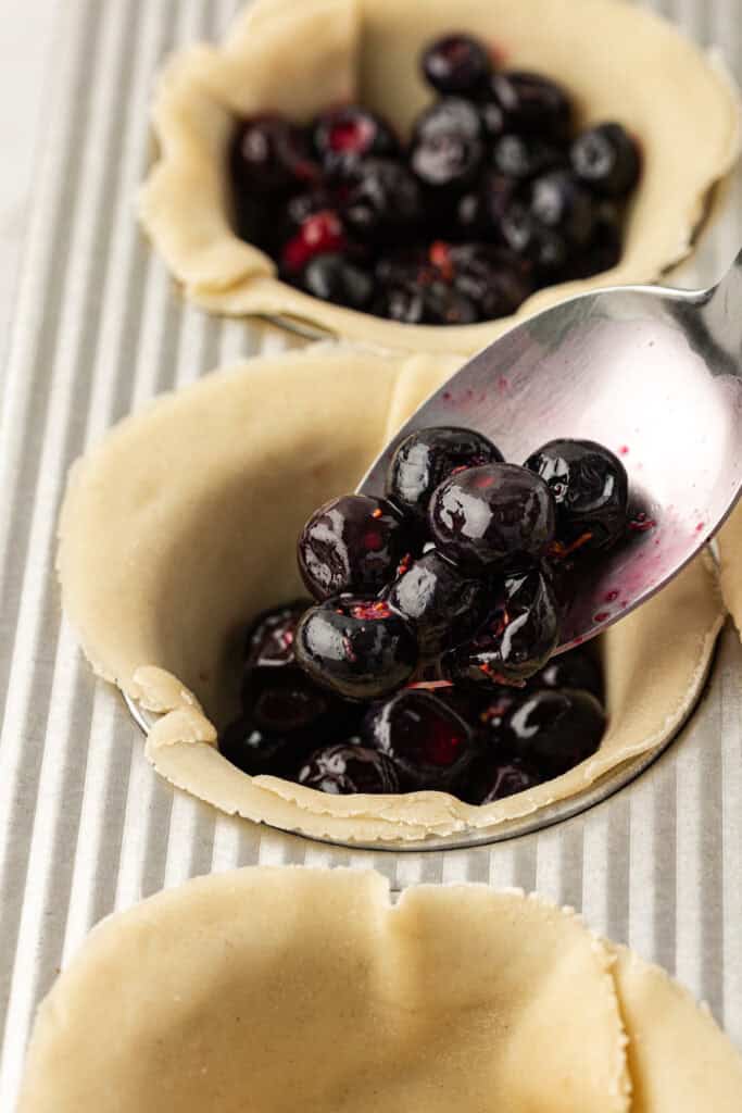 blueberry filling spooned into pie crust in muffin cups