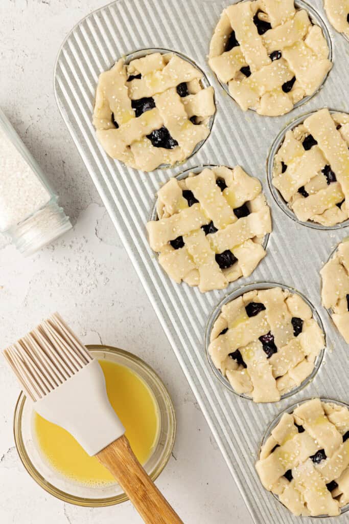 mini blueberry pies in a muffin tin with lattice tops and brushed with egg wash