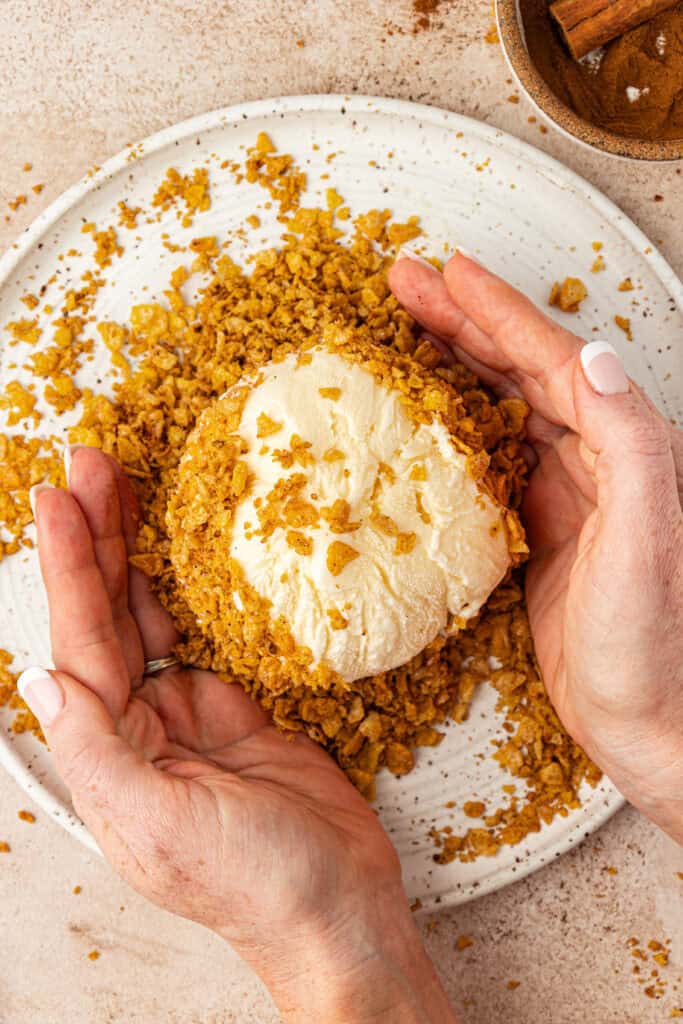 hands pressing the frosted flake mixture to the ice cream ball