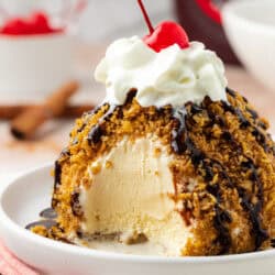 mexican fried ice cream on a plate topped with chocolate sauce, whipped cream and a cherry