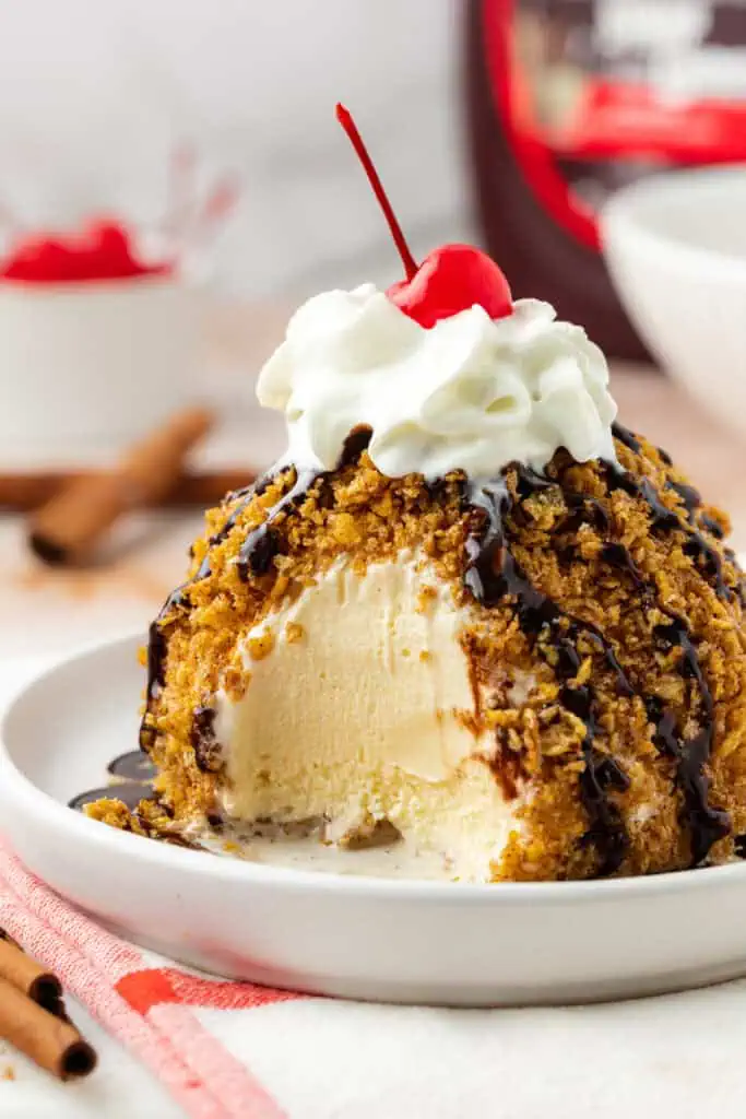mexican fried ice cream on a plate topped with chocolate sauce, whipped cream and a cherry