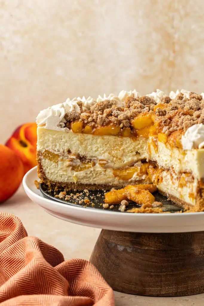 peach cobbler cheesecake on a cake stand with slice missing