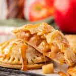 two apple hand pies stacked on each other covered in caramel sauce