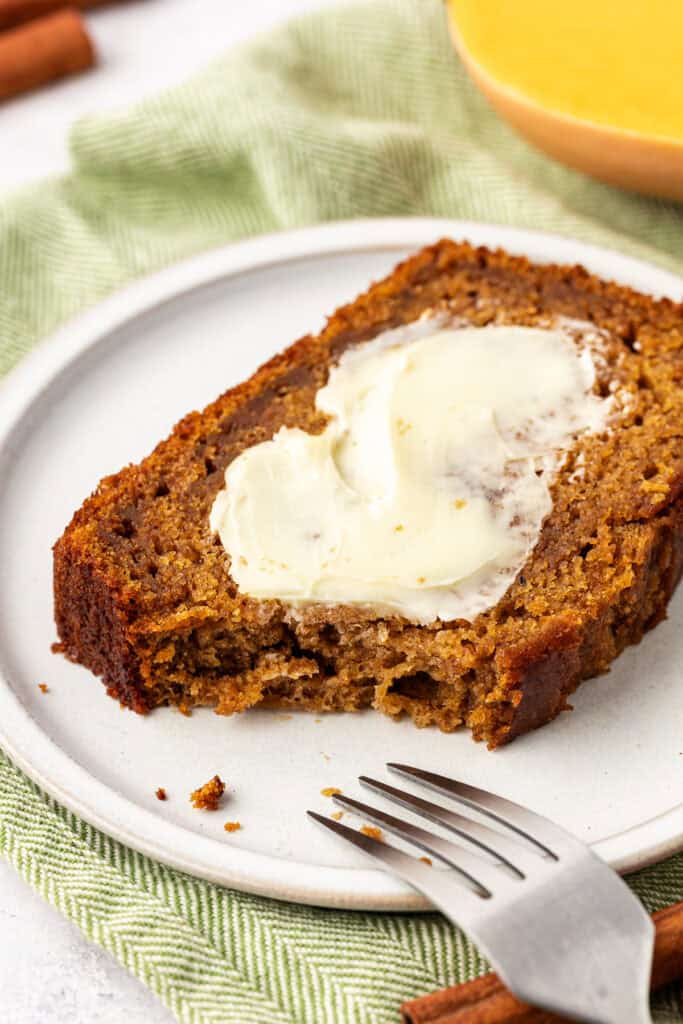 slice of butternut squash bread on a plate slathered in butter, and a bite missing