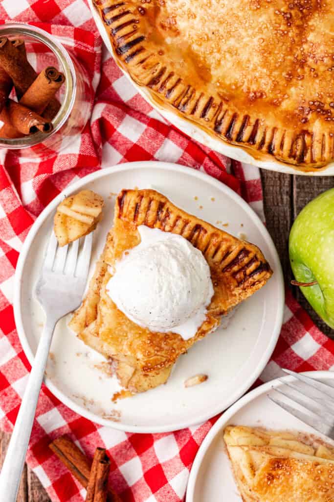 slice of apple pie on a plate topped with ice cream with a fork