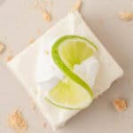 one key lime cheesecake bar on a plate topped with slice of lime